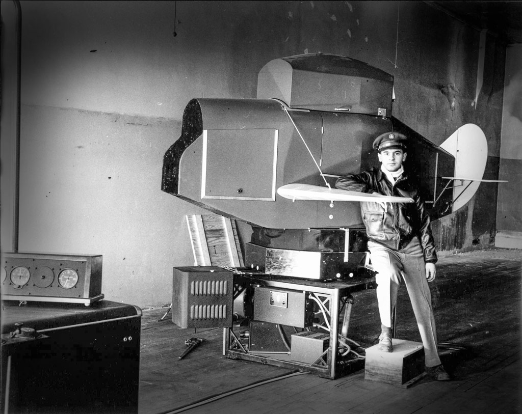 Flight instructor Paul Metcalf poses with an early flight simulator — called a Link trainer — used in Central’s ground school instruction.