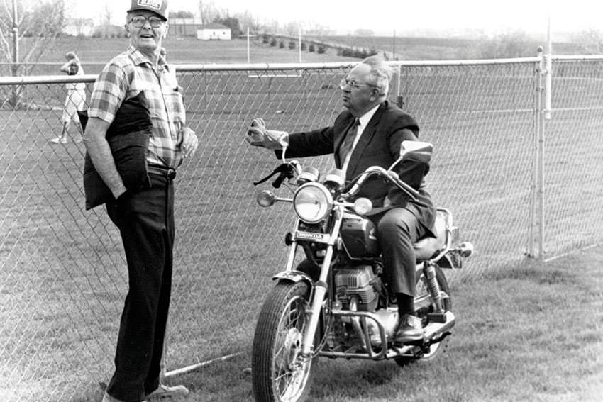 President Emeritus Ken Weller leans his motorcycle against the fence while watching a softball game following his retirement.��