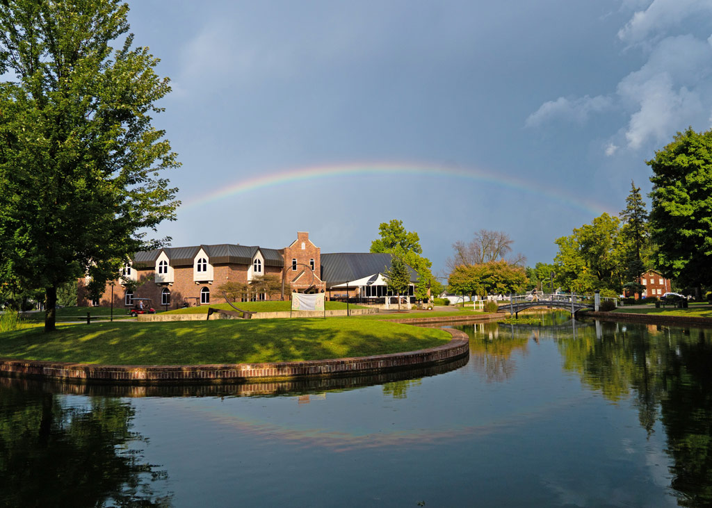 A glimmer of sunshine peeks through a darkened sky as a rainbow stretches over a quiet Maytag Student Center and peaceful pond on the east end of Central’s campus.